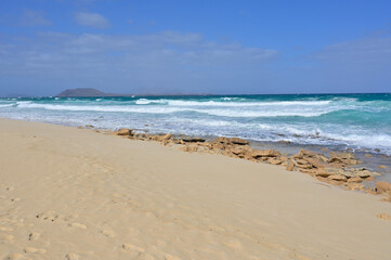 Corralejo beach showing turquoise ocean waves breaking on sand. Corralejo beach with clear blue sky and rolling turquoise waves on a sandy shore.