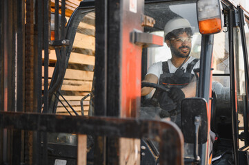 Warehouse worker driving forklift carrying lumber in timber warehouse