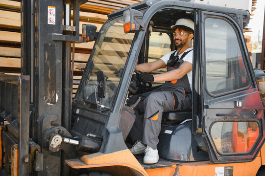 Warehouse worker driving forklift carrying lumber in timber yard - Powered by Adobe