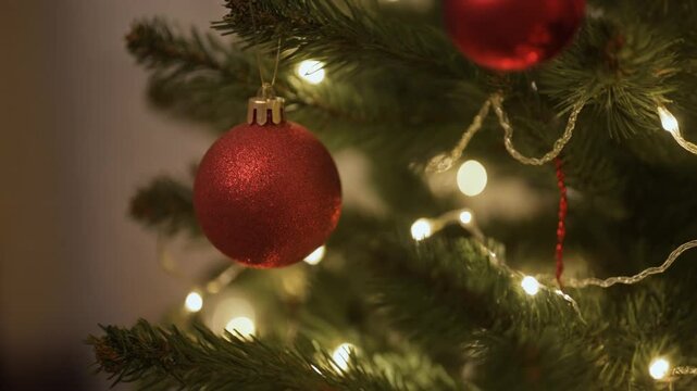 A close-up view of a festive Christmas tree adorned with shiny red baubles and twinkling warm white string lights, creating a cozy holiday atmosphere.
