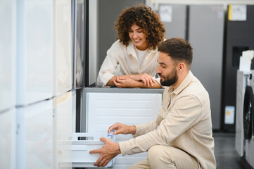Couple choosing refrigerator in electronics store, examining features together