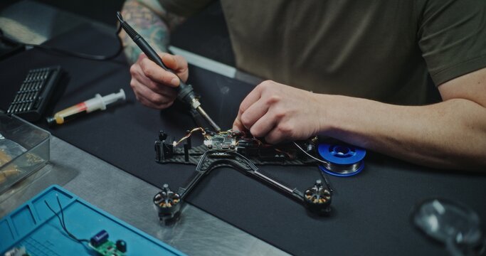 Close Up Engineer Working on Custom Electronic Solutions For Drone Platform. Man soldering Delicate Wires on Small Drones Controller. Problem Solving and Innovation Inherent in Drone RD and Design.