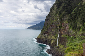 Naklejka premium Sea cliff waterfall Veu da Noiva on north coast of Madeira Island Portugal, tall cascade dropping from green rock walls into Atlantic