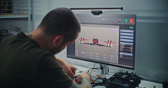 Male Engineer With Visible Tattoos Sits at Computer, Designing FPV Drone Model Using Specialized 3D Software For Drone Testing. Concept Technical Process Product Development and Digital Engineering.