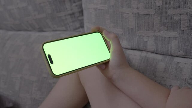 POV child hands watching videos on smartphone with green screen