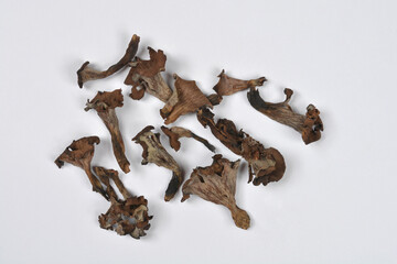 A scattered arrangement of dried, dark brown and gray Black Trumpet mushrooms is photographed from above on a white background