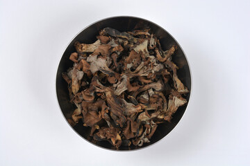 A metal bowl viewed from above is filled with dark brown and gray dried Black Trumpet mushrooms on a white background