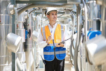 Technician writing on clipboard for checking pipeline valves or water tank area at urban industrial site