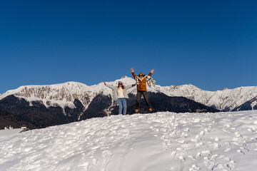 Couple Jumping Snow Mountains Winter: Joyful pair celebrates snowy mountaintop adventure during winter season.
