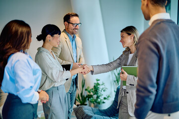 Group of diverse business colleagues meeting inside modern office building, shaking hands, starting new venture, and closing deal