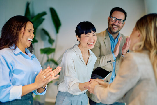 Multiracial business team congratulating diverse colleague with handshake and applause, celebrating collaboration and partnership - Powered by Adobe