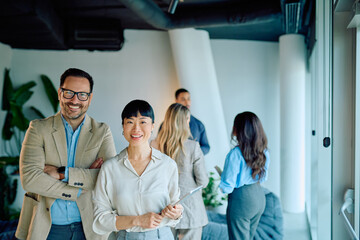Diverse business professionals smiling, looking at camera in a bright, contemporary office. Coworkers collaborating in the background