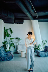 Businesswoman standing, working with a tablet in a contemporary office lounge, combining professional technology with a green interior