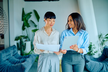 Two diverse businesswomen discussing documents and a digital tablet, collaborating on a project in...