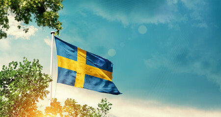 Sweden national flag waving in the sky behind the tree. The flag blowing with beautiful sunlight. Sweden national flag for independence day.