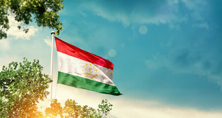 Tajikistan national flag waving in the sky behind the tree. The flag blowing with beautiful sunlight. Tajikistan national flag for independence day.