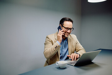 Happy businessman making a phone call, smiling while typing on laptop keyboard, drinking coffee and managing tasks