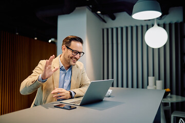 Happy businessman using laptop for video conferencing and online communication, working remotely, smiling while greeting