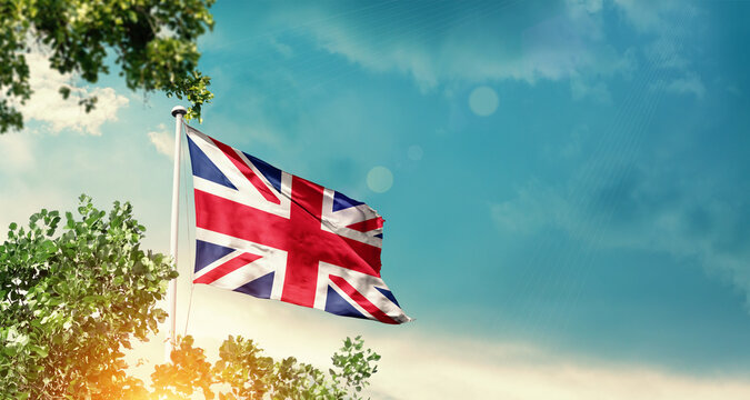 United Kingdom national flag waving in the sky behind the tree. The flag blowing with beautiful sunlight. UK national flag for independence day.