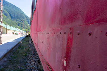 Close-up of the weathered red side of an old train carriage towards a mountain landscape