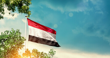 Yemen national flag waving in the sky behind the tree. The flag blowing with beautiful sunlight. Yemen national flag for independence day.