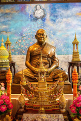 Obraz premium A radiant golden Buddha statue seated on a decorated altar inside a Thai temple with ornate offerings and a heavenly mural backdrop.