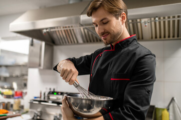 Professional chef whisking ingredients in metal bowl in kitchen