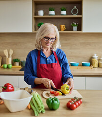 Portrait of happy senior mature woman prepering meal with fresh vegatebles in kitchen
