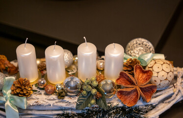 Advent wreath with four white candles and elegant Christmas decorations. Close-up holiday centerpiece with ornaments, pinecones and natural elements on a rustic base.