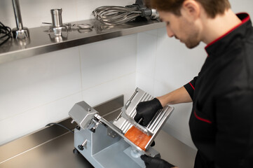 Man in uniform slicing meat with professional slicer