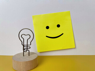 Positive mindset concept with a smiley face sticky note and a light bulb idea symbol.