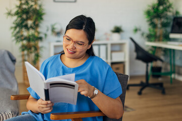 A lady engrossed in a book sits comfortably, radiating happiness in a stylish, modern interior filled with natural light, greenery, and beautiful decor elements around her.