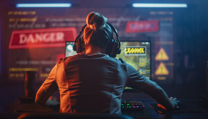 Woman with headphones playing video game on computer in dimly lit room.