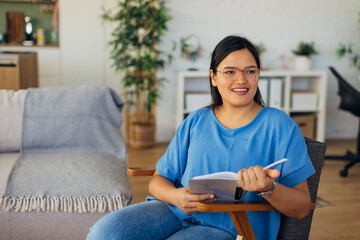 In a stylish living room with natural decor, a woman enjoys reading her book, creating a serene atmosphere that merges comfort, modern aesthetics, and personal joy.