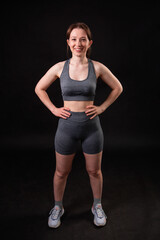 Portrait of attractive young fitness woman in grey top and shorts posing isolated on black background.