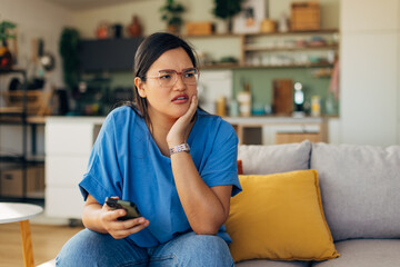 In a chic and bright living room, a young woman shows emotional engagement while checking her phone, creating a captivating portrait of modern lifestyle and connection.