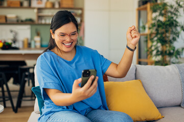 A happy woman is captured mid-laughter as she interacts with her mobile device, surrounded by inviting colors and a chic, modern interior design.