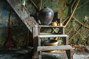 Old wooden staircase corner with traditional jars, gourds, and rustic household items inside an abandoned Chinese house in Papan Heritage Village, Perak, Malaysia