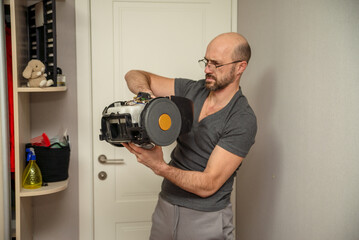 Focused man in glasses fixing a broken vacuum cleaner at home. This image captures the challenge and satisfaction of DIY appliance repair, highlighting a common household task and problem-solving skil
