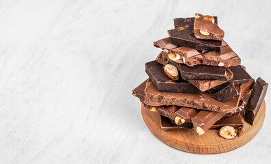 Assorted pieces of dark and milk chocolate with nuts stacked on light background copy space, perfect for dessert concepts, confectionery advertising and sweet food layouts