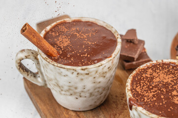 Hot thick chocolate served in a rustic ceramic mug with cinnamon and cocoa powder sprinkled on top, surrounded by chocolate pieces for a cozy dessert concept and warm winter food styling.