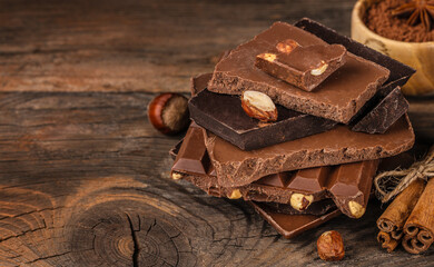 Stack of assorted chocolate bars with nuts on a rustic wooden background, creating a warm cozy dessert atmosphere perfect for food advertising and sweet product branding.