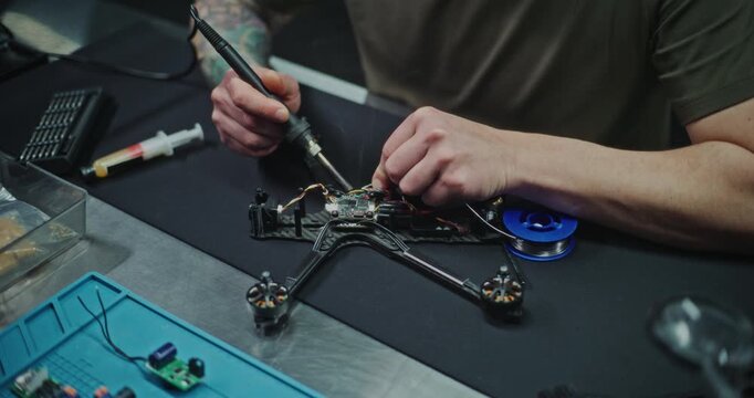 Close Up Engineer Working on Custom Electronic Solutions For Drone Platform. Man soldering Delicate Wires on Small Drones Controller. Problem Solving and Innovation Inherent in Drone RD and Design.