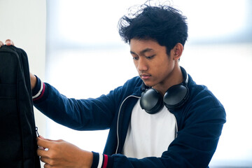 Young Asian Student Male zipping backpack with headphones ready for musician school