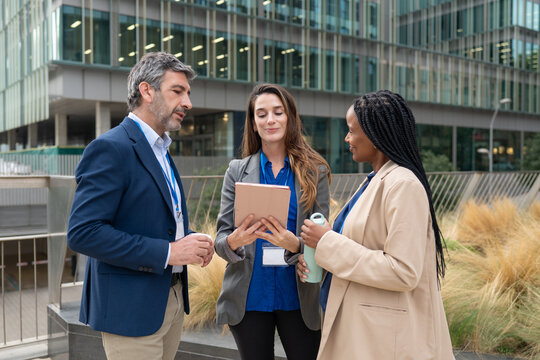Diverse business professionals discussing work using digital tablet outdoors