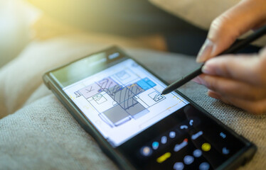 Fototapeta premium Digital floor plan sketching and editing on smartphone with stylus, Hand using stylus to draw, edit digital floor plan on smartphone, showing modern mobile design, creativity, and home planning tools