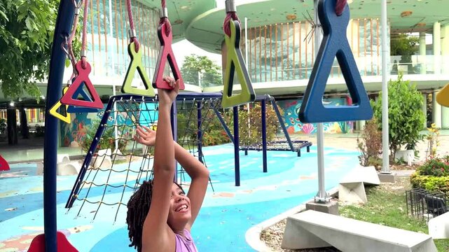 Smiling african american girl happily climbing on hanging rings at an outdoor playground on a sunny day