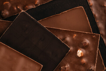Close-up assortment of layered dark, milk and nut chocolate bars stacked together, captured in warm macro lighting without copy space, ideal for confectionery advertising, dessert branding