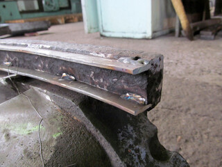 Close-up of a metal component with visible welding spots, suggesting repair or fabrication. The rough, textured surface of the metal. Industrial setting. Restoration of diaphragms