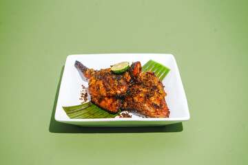 Grilled chicken ayam bakar with crispy spiced skin, lime on baanana leaf and white plate